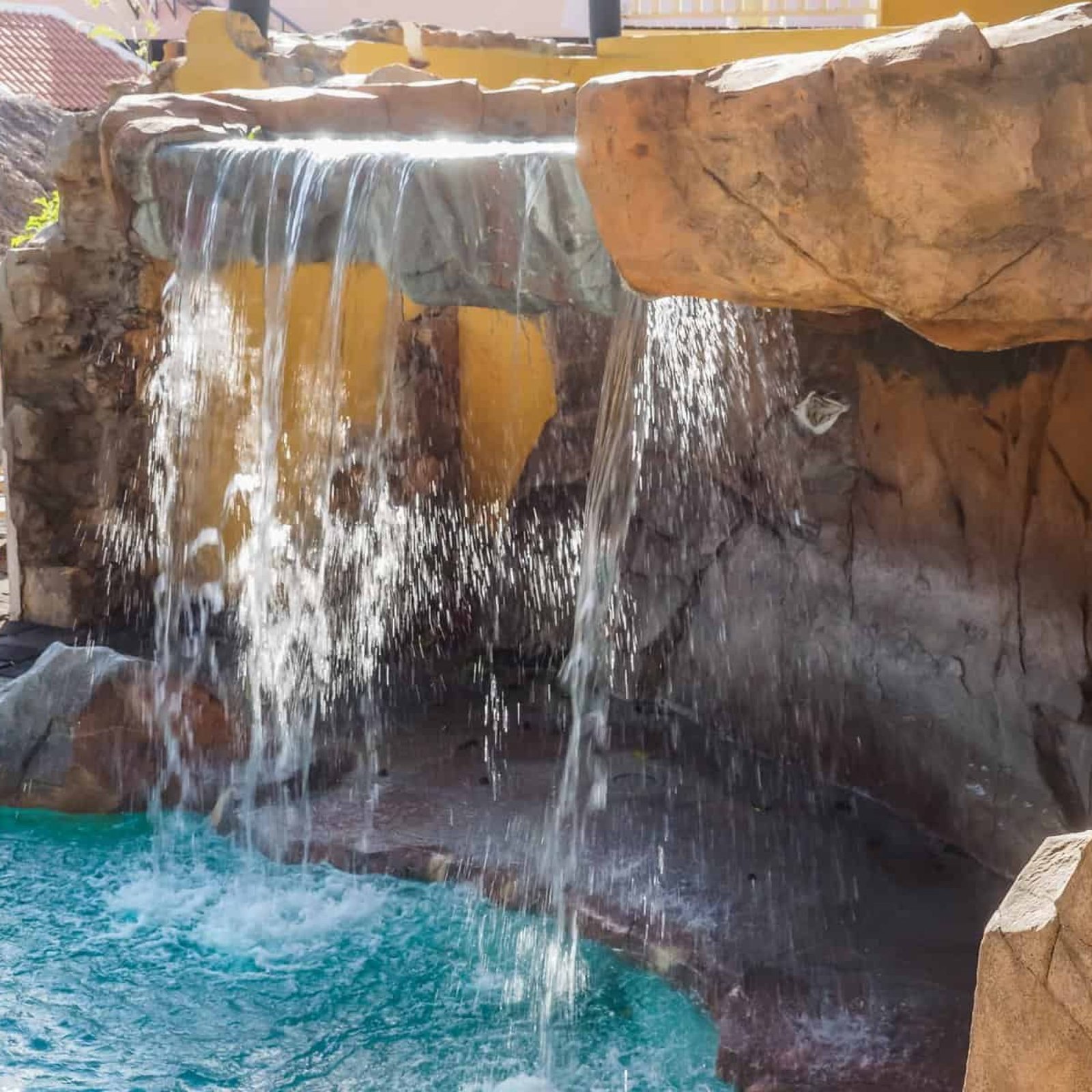 Waterfall feature in a backyard pool with rocks and water cascading down.